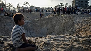 Palestinians look at the destruction after an Israeli airstrike on a crowded tent camp in Muwasi.