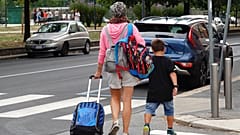 Uma mulher carrega mochilas enquanto o seu filho caminha depois de sair de uma escola primária, em Milão, Itália, quarta-feira, 14 de setembro de 2022.