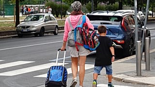 Uma mulher carrega mochilas enquanto o seu filho caminha depois de sair de uma escola primária, em Milão, Itália, quarta-feira, 14 de setembro de 2022.