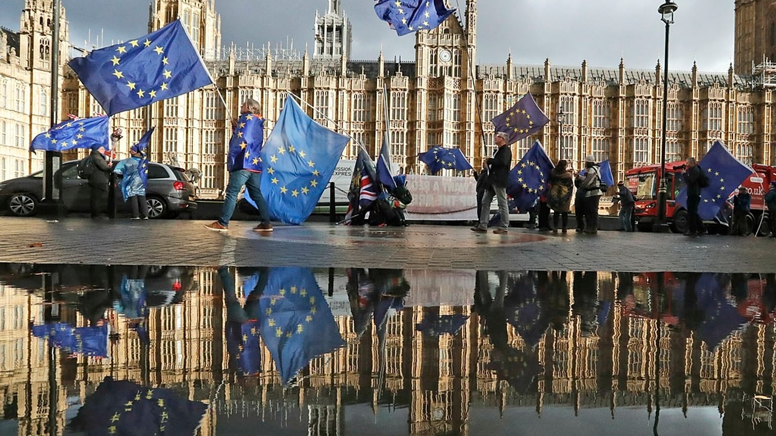 Protestors are reflected in a large puddle as they wave European flags to demonstrate against Brexit in front of the Parliament in London, Dec. 3, 2018.