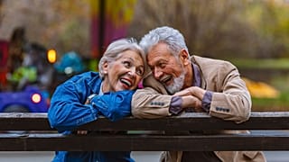 A happy senior couple sitting on a park bench, looking at each other