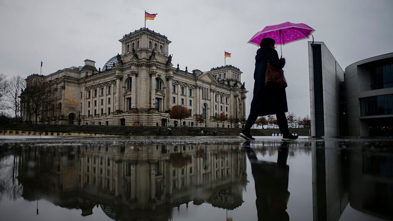 A person with an umbrella walks through the government district in front of the Reichstag building, the house of German parliament Bundestag,in Berlin, Germany, 2022.