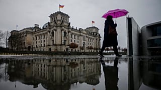 A person with an umbrella walks through the government district in front of the Reichstag building, the house of German parliament Bundestag,in Berlin, Germany, 2022.