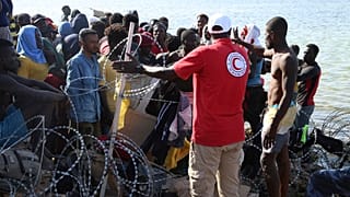 مهاجرون يتجمعون بالقرب من الحدود الليبية التونسية بينما تقوم قوات الأمن الليبية وعمال الصليب الأحمر الليبي بتوزيع المساعدات الغذائية عليهم 23 تموز يوليو 2023