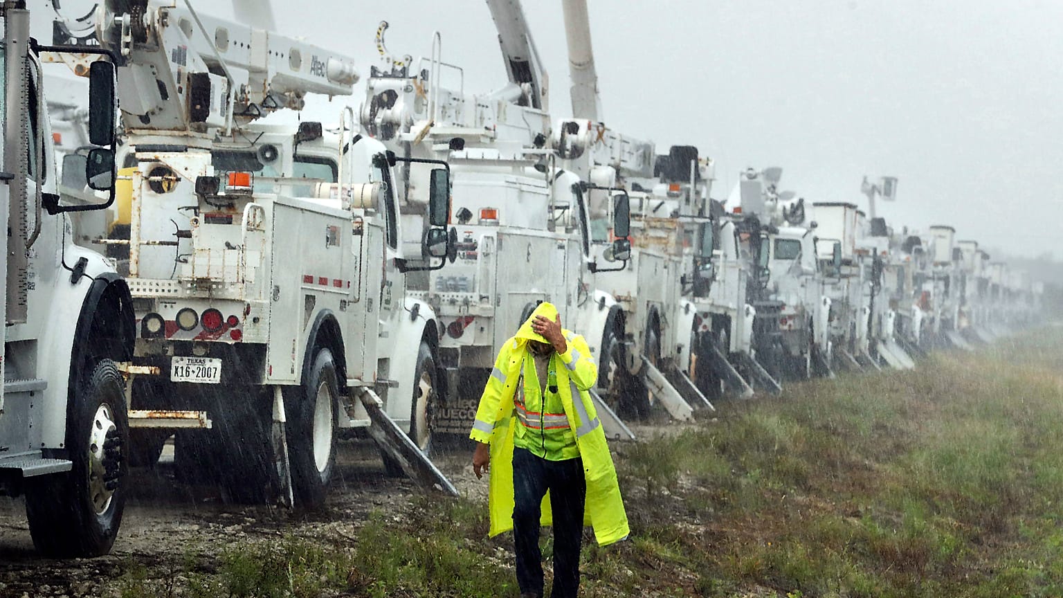 Bir vatandaş Helene Kasırgası'nın yol açacağı hasara hazırlık amacıyla bir tarlada bulunan elektrik hattı kamyonlarının yanından geçerken yağmur altında kalıyor, 26 Eylül 2024
