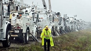 Bir vatandaş Helene Kasırgası'nın yol açacağı hasara hazırlık amacıyla bir tarlada bulunan elektrik hattı kamyonlarının yanından geçerken yağmur altında kalıyor, 26 Eylül 2024