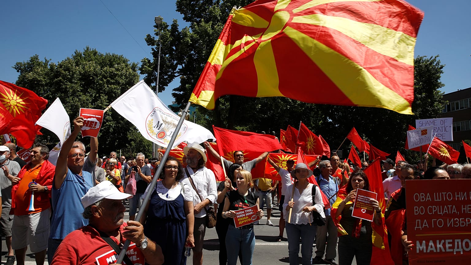 Le persone tengono in mano la vecchia e l'attuale bandiera nazionale e cantano slogan durante una protesta davanti al palazzo del Parlamento a Skopje, il 14 luglio 2022.