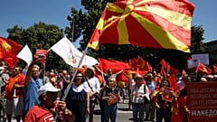 Varias personas sostienen las banderas nacionales antigua y actual y corean eslóganes durante una protesta frente al edificio del Parlamento en Skopje, 14 de julio de 2022.