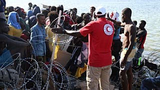 مهاجرون يتجمعون بالقرب من الحدود الليبية التونسية، بينما تقوم قوات الأمن الليبية وعمال الصليب الأحمر الليبي بتوزيع المساعدات الغذائية عليهم يوم الأحد 23 يوليو 2023