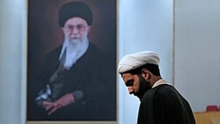 یک روحانی هوادار حکومت ایران در برابر عکس علی خامنه‌ای، رهبر جمهوری اسلامی