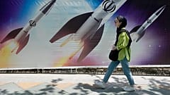 فایل: زنی در شمال تهران، ۱۹ آوریل ۲۰۲۴، از روی پرچمی که نشان می دهد موشک های پرتاب شده عبور می کند