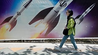 ARQUIVO: Uma mulher passa por um cartaz que mostra mísseis a serem lançados, no norte de Teerão, a 19 de abril de 2024