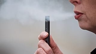 A woman exhales a puff of vapor from an e-cigarette in 2019.