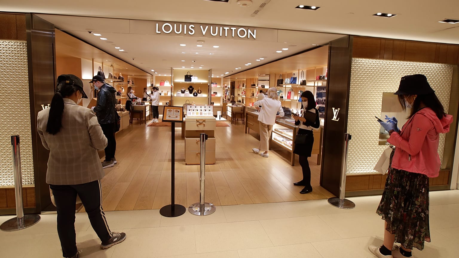 Customers wait in front of a luxury shop in Milan, Italy, Monday, May 18, 2020. Italy is slowly lifting sanitary restrictions after a two-month coronavirus lockdown. 