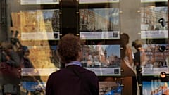 Ένας άνδρας κοιτάζει μια βιτρίνα ακινήτων στο παράθυρο ενός μεσιτικού γραφείου 