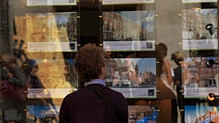 Ένας άνδρας κοιτάζει μια βιτρίνα ακινήτων στο παράθυρο ενός μεσιτικού γραφείου 