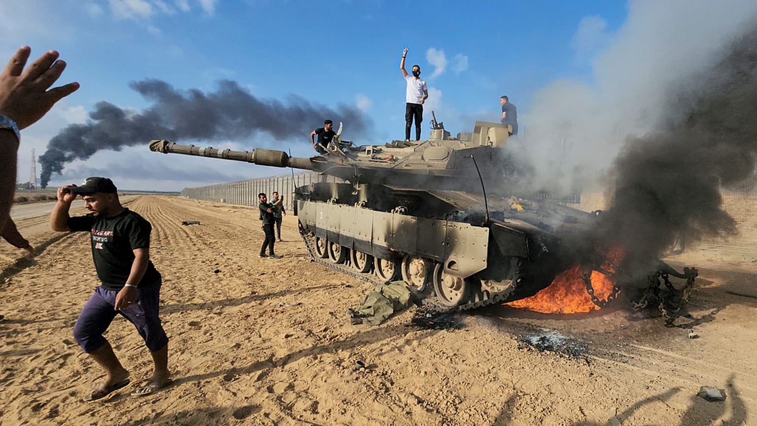   فلسطينيون يحتلفون فوق دبابة محترقة في يوم 7 أكتوبر/ تشرين الأول 2023. 