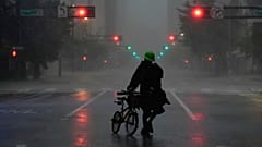 Ron Rook, who said he was looking for people in need of help or debris to clear, walks through windy and rainy conditions on a deserted street in downtown Tampa, Fla.