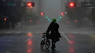 Ron Rook, who said he was looking for people in need of help or debris to clear, walks through windy and rainy conditions on a deserted street in downtown Tampa, Fla.