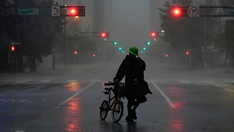 Ron Rook, who said he was looking for people in need of help or debris to clear, walks through windy and rainy conditions on a deserted street in downtown Tampa, Fla.