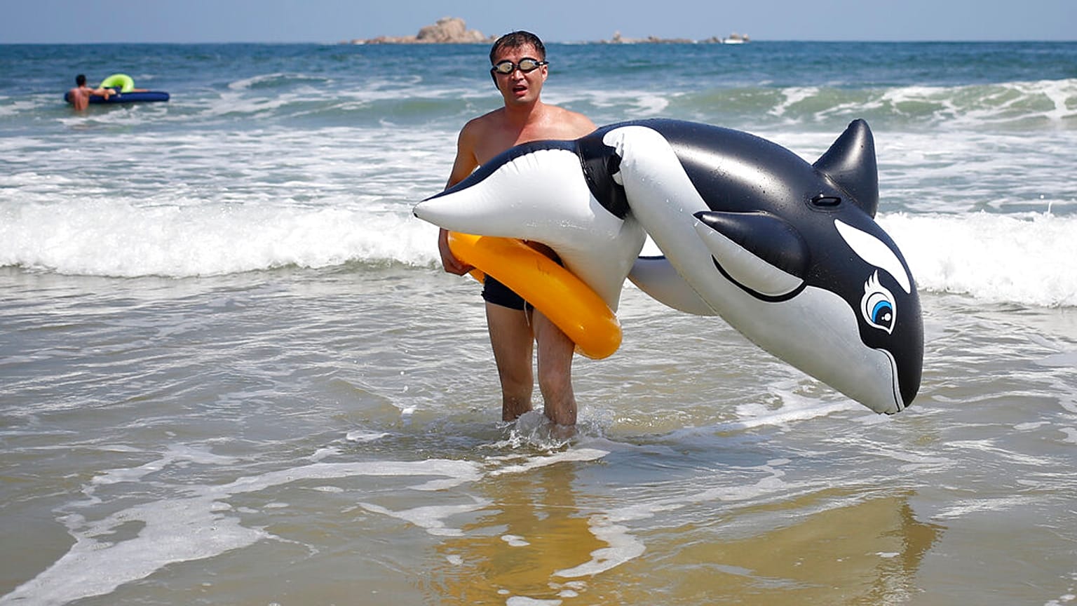 Un uomo cammina con un'orca gonfiabile sulla spiaggia di Sijung Ho in Corea del Nord prima della pandemia e della chiusura delle frontiere