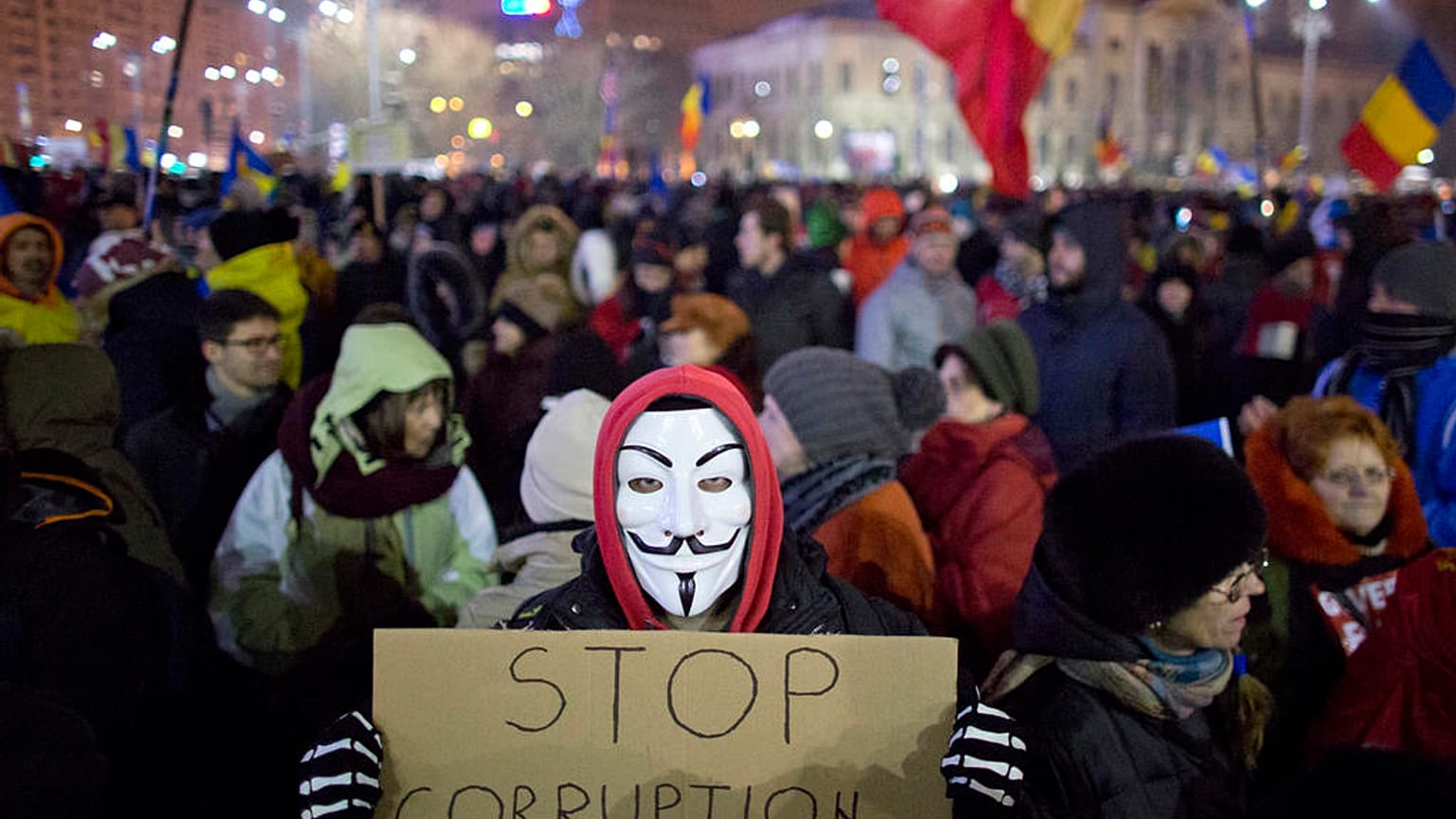 A masked protester holds a banner during a demonstration in Bucharest, Romania, Sunday, Feb. 12, 2017.