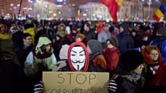 A masked protester holds a banner during a demonstration in Bucharest, Romania, Sunday, Feb. 12, 2017.