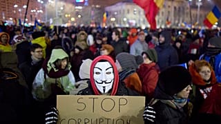 A masked protester holds a banner during a demonstration in Bucharest, Romania, Sunday, Feb. 12, 2017.