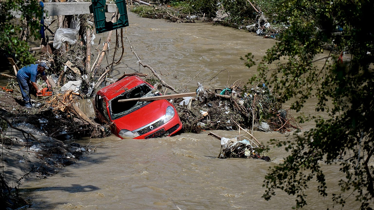 Un hombre utiliza una motosierra para cortar tocones de árboles para liberar un coche arrastrado por la reciente inundación en Arges, 30 de julio de 2024.