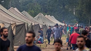 مهاجرون يسيرون داخل مخيم اللاجئين الذي تم بناؤه حديثًا في ساحة التدريب العسكرية في رودينكاي، على بعد حوالي 38 كيلومترًا (23.6 ميلًا) جنوب فيلنيوس، ليتوانيا، الأربعاء 4 أغسطس 
