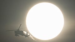 An Israeli Apache helicopter flies past the sun, near the Israeli-Lebanon border, as seen from northern Israel, 13 October 2024