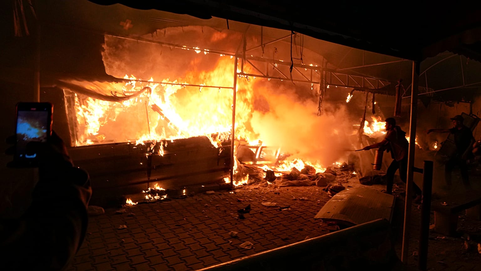 Palestinians try to extinguish fire caused by an Israeli strike that hit a tent area in the courtyard of Al Aqsa Martyrs hospital in Deir al-Balah
