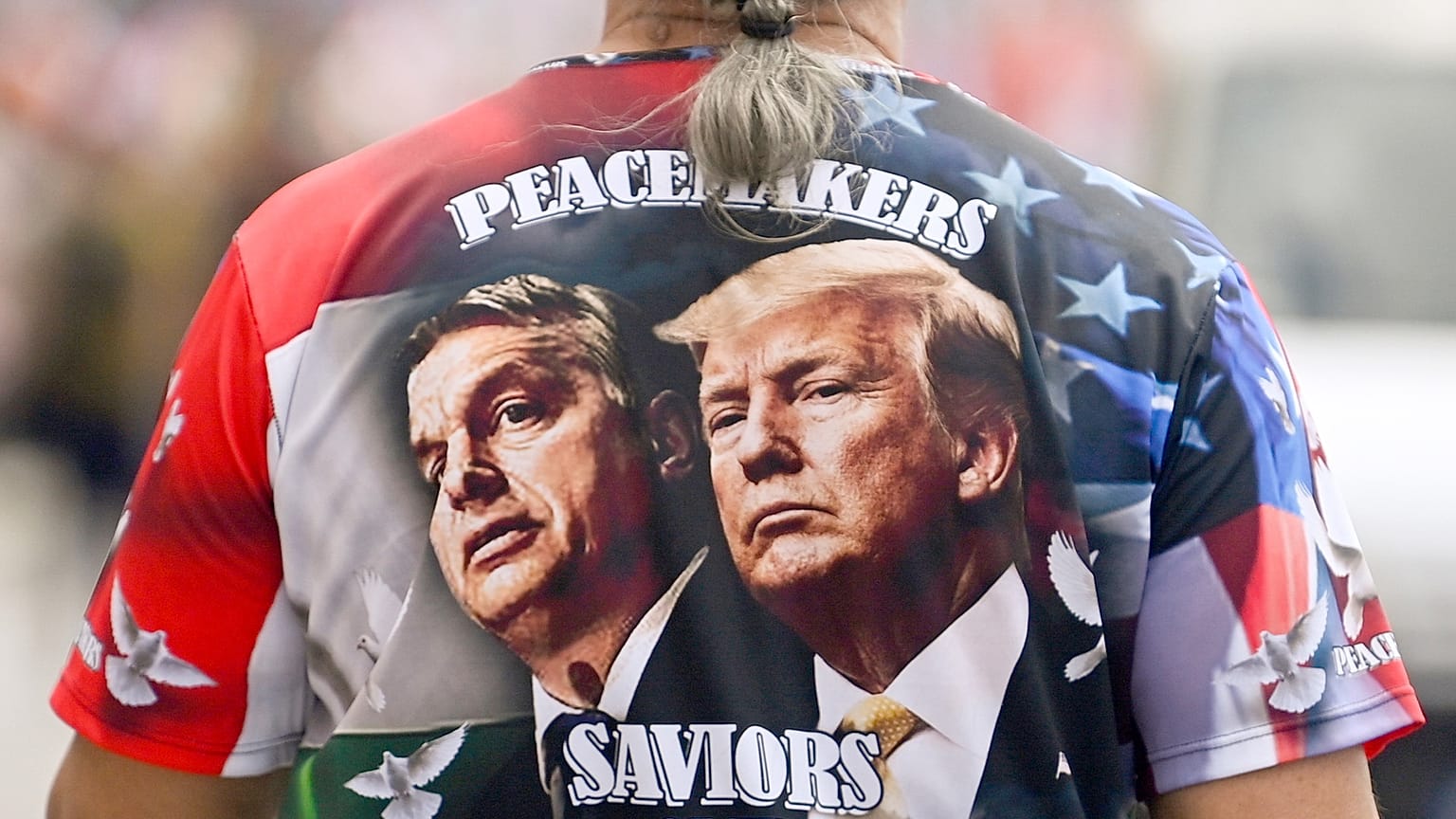 Um homem exibe uma t-shirt com os rostos do primeiro-ministro da Hungria, Viktor Orbàn, à esquerda, e de Donald Trump, enquanto participa numa marcha, em Budapeste, a 1 de junho de 2024