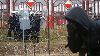 Białoruscy żołnierze, po lewej, stoją na straży, gdy migranci z Bliskiego Wschodu i innych miejsc gromadzą się na granicy białorusko-polskiej w pobliżu Grodna na Białorusi