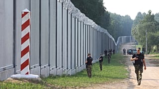 ARQUIVO - Guardas fronteiriços polacos patrulham um muro de metal na fronteira entre a Polónia e a Bielorrússia, perto de Kuznice, na Polónia.