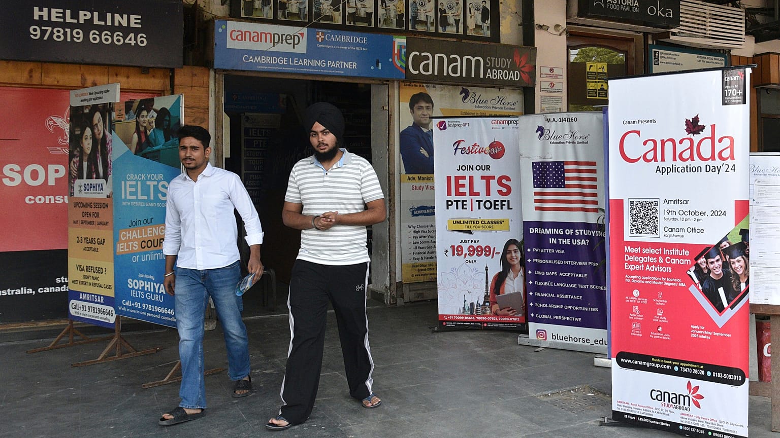 Hindistan'ın kuzeyindeki Pencap eyaletine bağlı Amritsar'daki bir pazarda, öğrencileri Kanada ve diğer ülkelerde okumaya davet eden pankartların önünden geçiyor, 15 Ekim 2024 