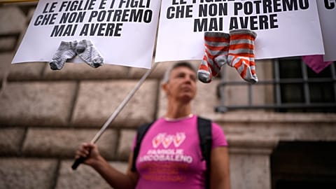 Banners reading "The daughters and sons we could never have" and pairs of toddler socks are shown during a pro-surrogacy press conference in Rome, Tuesday, Oct.15, 2024. 