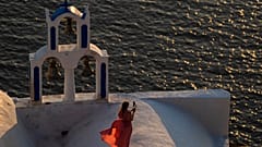 A woman takes pictures as she stands on the top of a Greek Orthodox Church while the sun sets in the Aegean Sea, in Santorini