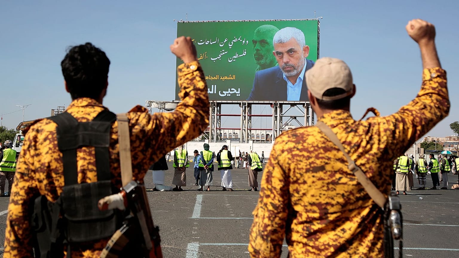 دو سرباز یمنی در حال شعار دادن مقابل بیلبوردی با تصویر سنوار در تاریخ ۱۸ اکتبر ۲۰۲۴