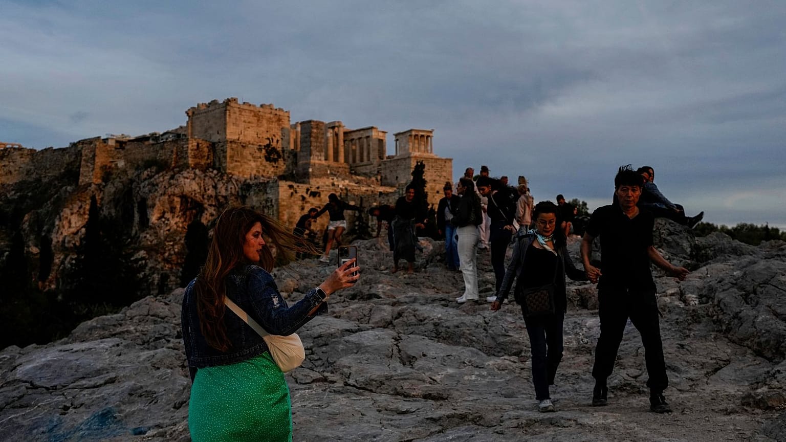 Turisti passeggiano sulla collina dell'Areopago, di fronte all'antica Acropoli, mentre il sole tramonta ad Atene.