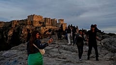 Turistas caminham na colina do Areópago, em frente à antiga Acrópole, enquanto o sol se põe em Atenas.