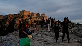 Turisti passeggiano sulla collina dell'Areopago, di fronte all'antica Acropoli, mentre il sole tramonta ad Atene.