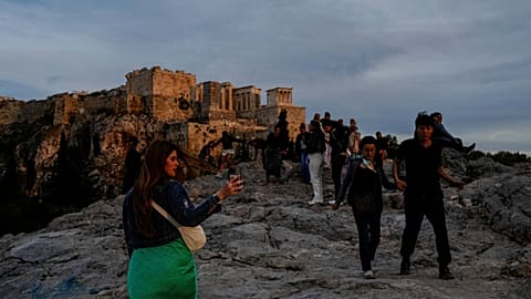Tourists walk at Areopagus hill in front of the Ancient Acropolis hill as the sun sets in Athens.