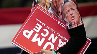 Um apoiante carrega cartazes depois de o candidato presidencial republicano, o ex-presidente Donald Trump, ter discursado num comício de campanha na Williams Arena do Coliseu de Mignes, 21 de outubro de 2024