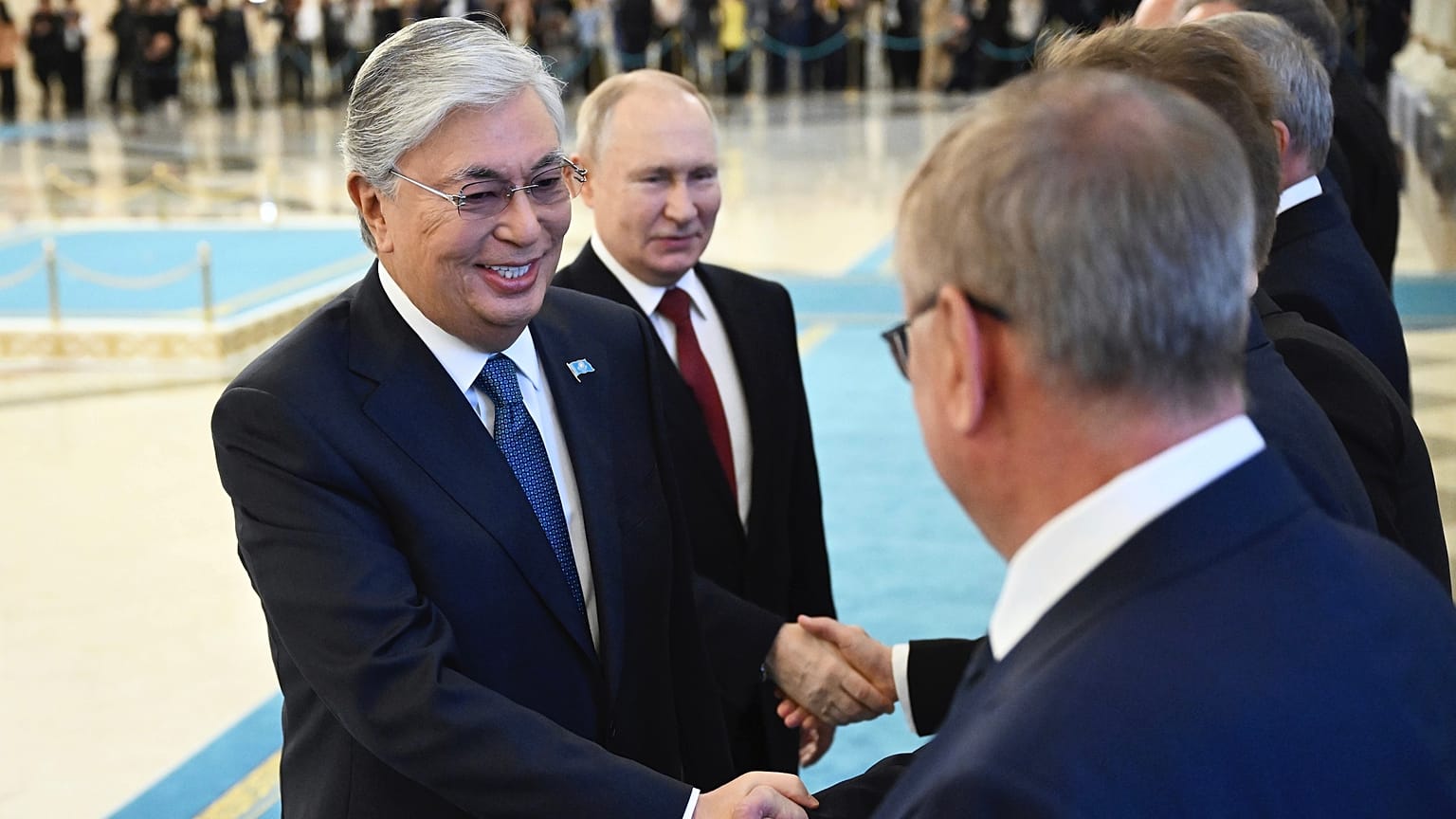 Kasım Cömert Tokayev (solda) ve Vladimir Putin (ortada), Kazakistan'ın başkenti Astana'da düzenlenen törende diplomatlarla el  sıkışıyor, 9 Kasım 2023.