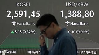 A currency trader works near a screen showing the Korea Composite Stock Price Index (KOSPI).
