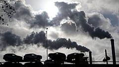 De la fumée s'élève d'une usine alors qu'un camion chargé de voitures traverse un pont à Paris, en France.