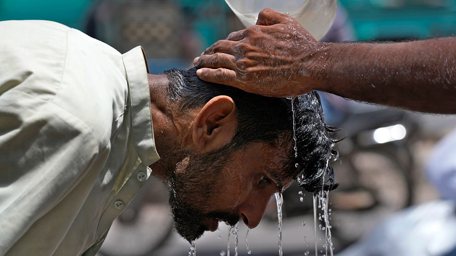 Ein Freiwilliger gießt einem Mann Wasser über den Kopf, um sich an einem heißen Sommertag in Karachi, Pakistan, abzukühlen