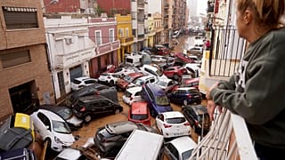 A woman looks out from her balcony as vehicles are trapped in the street during flooding in Valencia