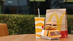 Bu fotoğrafta McDonald's markasına ait bir hamburger, içecek ve paket görülüyor